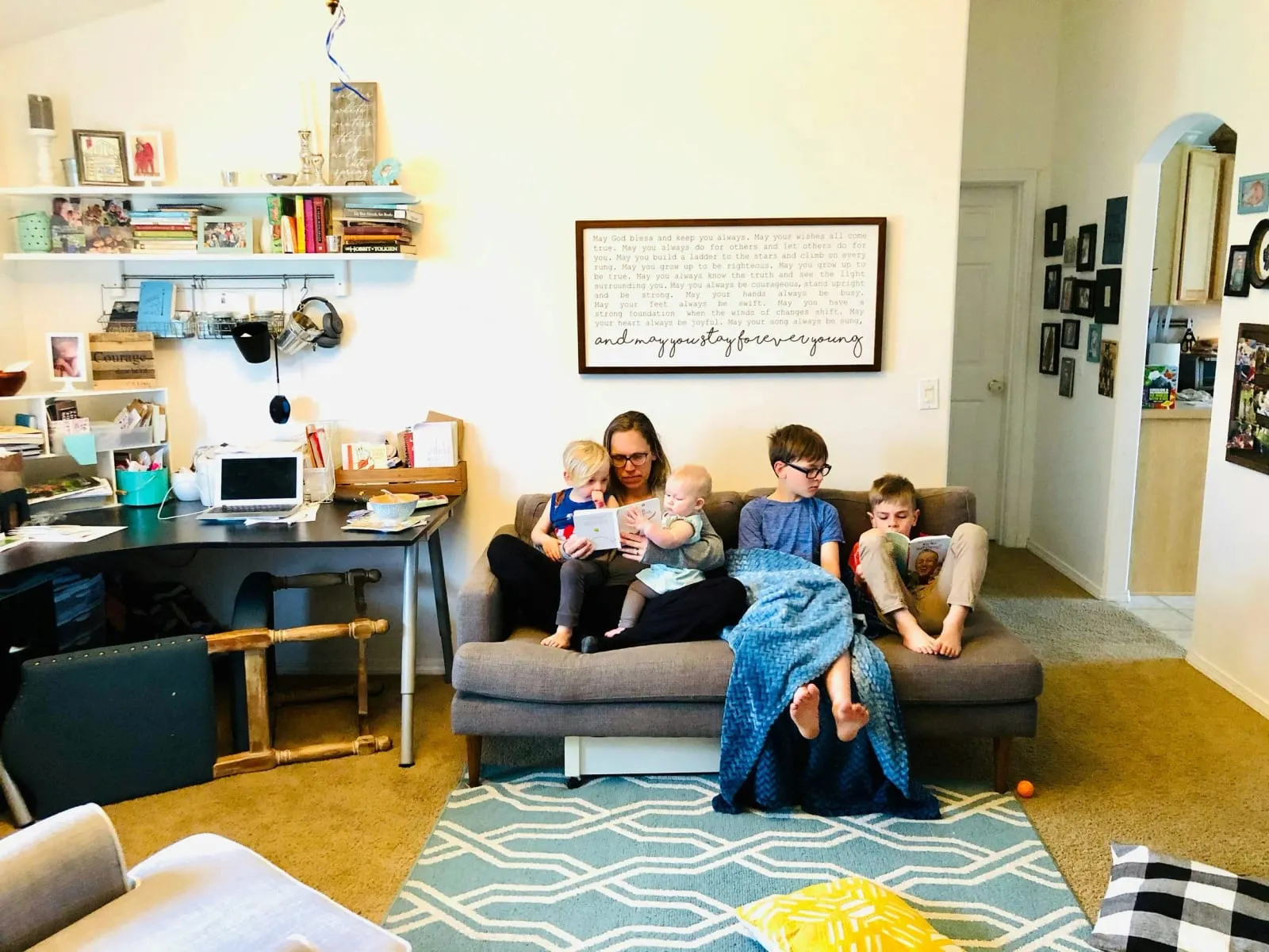 Eine Mutter liest mit vier Kindern auf dem Sofa im Wohnzimmer.