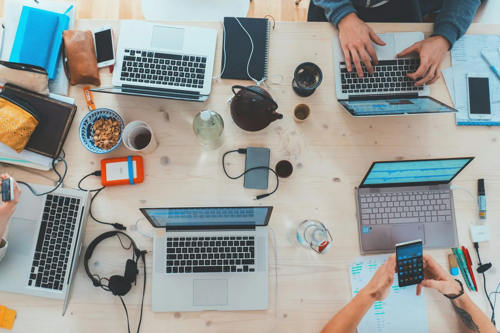 Ein Arbeitstisch von oben mit mehreren Laptops, Kopfhörern und Notizen.
