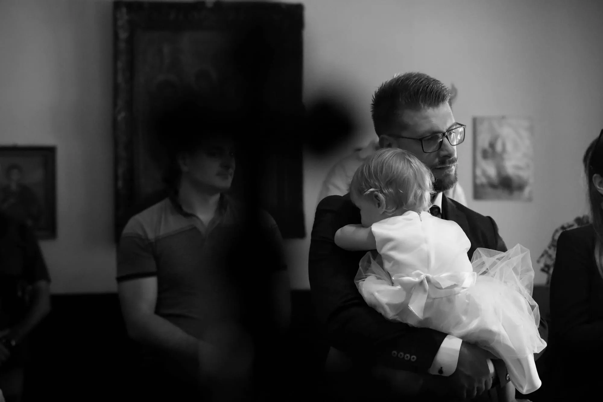 Schwarz-Weiß-Foto: Ein Mann im Anzug hält ein Baby im weißen Kleid auf dem Arm.